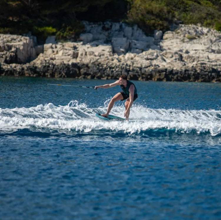 Person wakeboarding on a body of water with rocky cliffs in the background